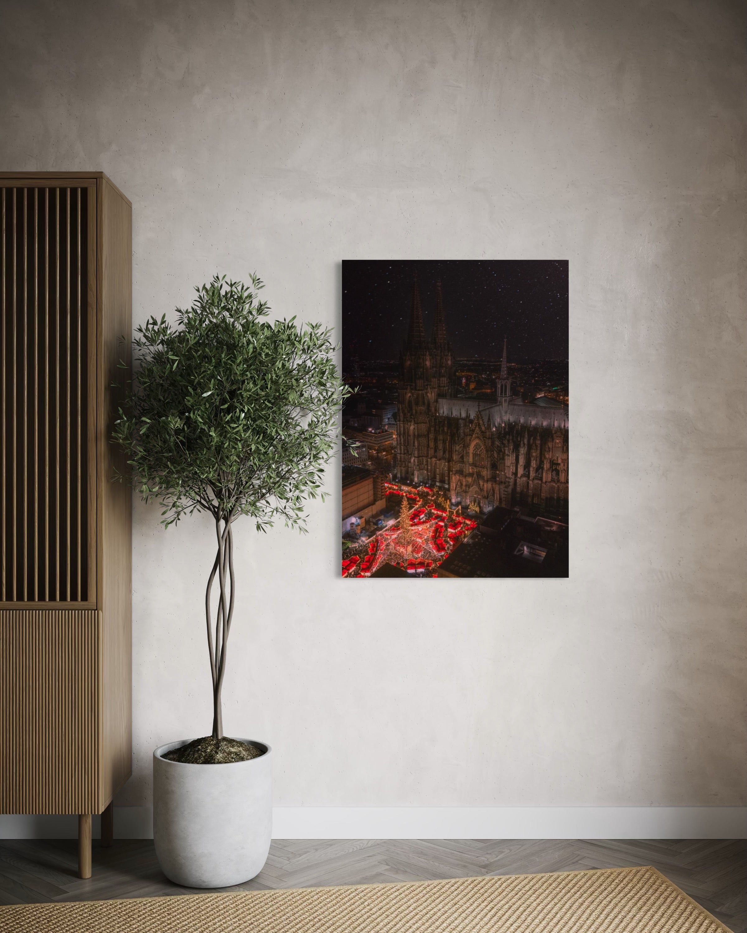 Framed artwork of a cityscape on a wall next to a potted plant and wooden cabinet.